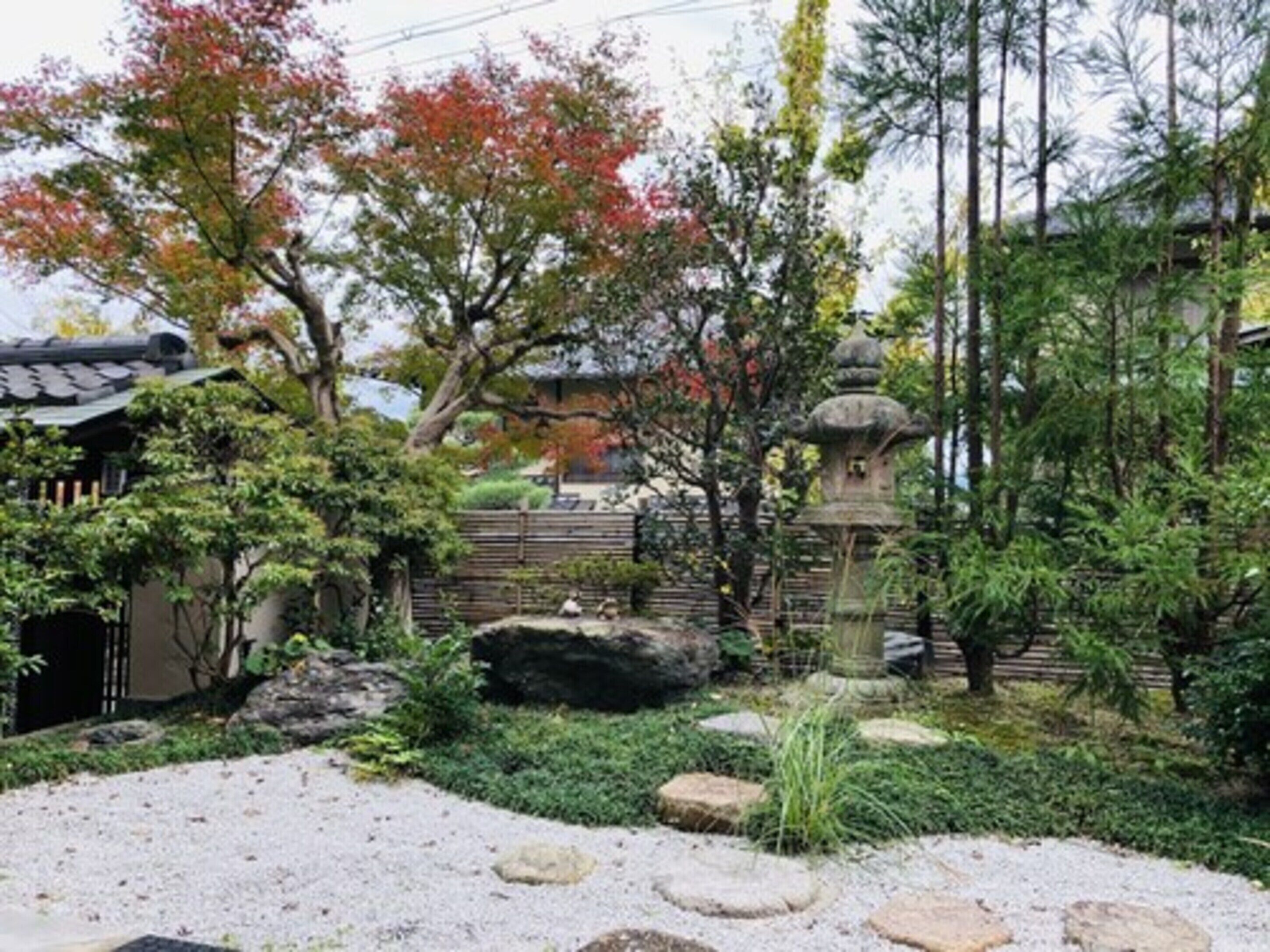 Um jardim japonês tradicional com um lampião de pedra, formações rochosas e um edifício de madeira.