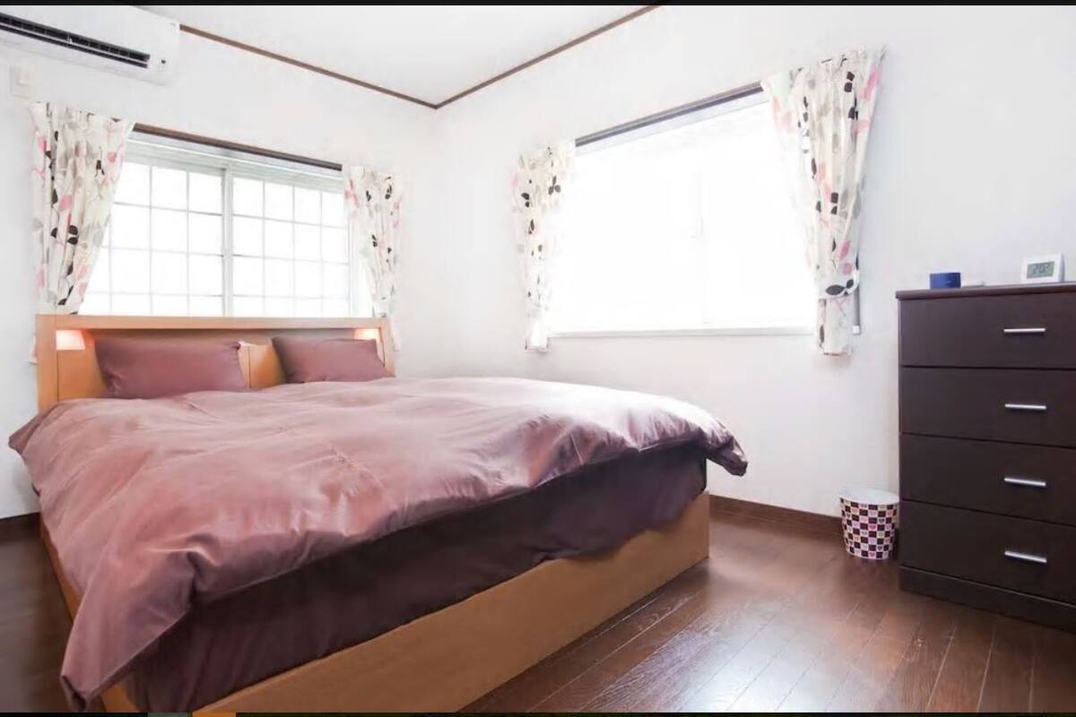 Een slaapkamer met een bed, een kapstok en een raam met gordijnen.