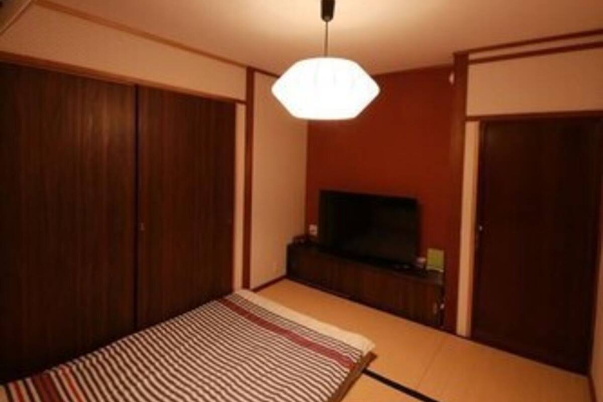 Een kamer met een tatami mat, een lage houten tafel, een televisie op een kast en een hangende lamp.