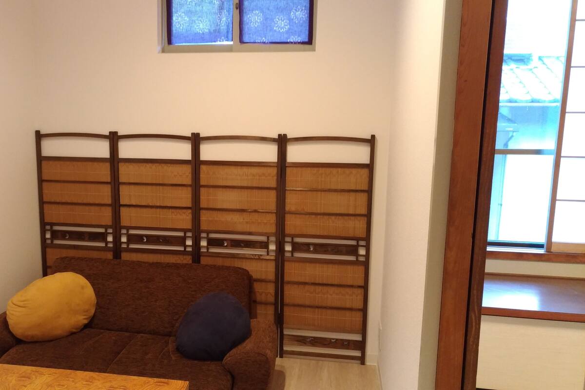 Een kamer met een bruine bank, twee kussens, een houten hoofdbord en een raam met behang.