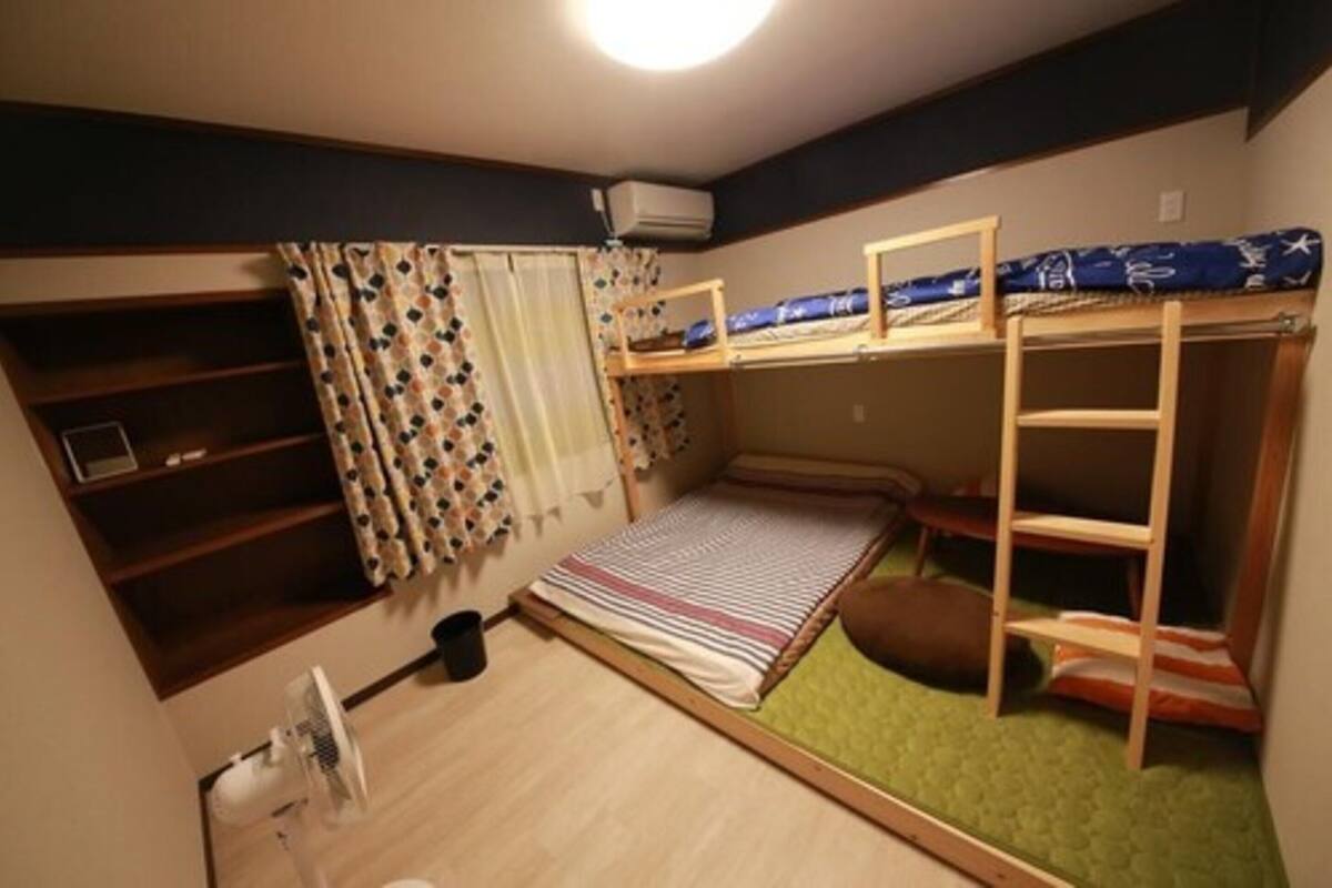 Een kleine kamer met stapelbedden, een bureau en een ventilator.