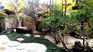 A traditional Japanese garden with a stone lantern, rock formations, and a variety of plants. - Kinkaku Ryokan (Kyoto)