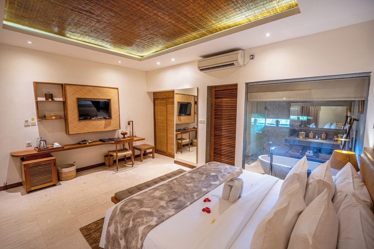 A modern hotel room with a large bed, a desk, a television, and a bathroom with a bathtub and shower.