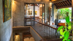 A staircase with a metal railing, a wooden ceiling, and a view of a dining area with tables and chairs. - Purana Suite Ubud (Ubud)