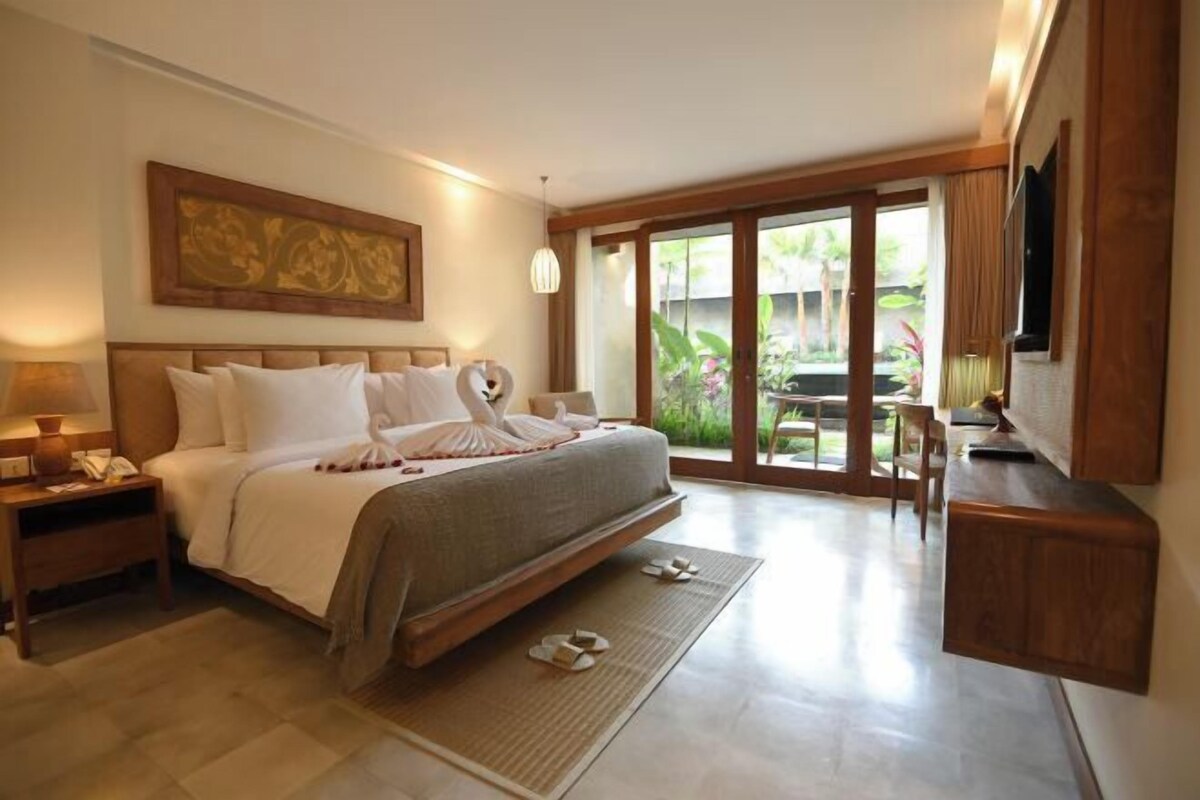 A spacious bedroom with a large bed, a bedside table, a desk, and a TV.