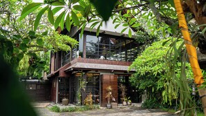 A modern building with large windows, surrounded by lush greenery. - Purana Suite Ubud (Ubud)