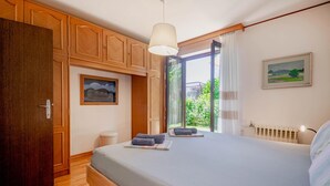 Une chambre avec un grand lit, une armoire en bois et une fenêtre donnant sur un paysage verdoyant.