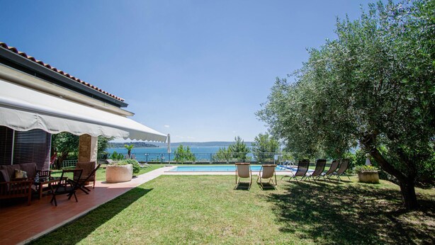 Un espace aménagé au bord de la piscine, avec vue sur la mer, comprenant du mobilier d’extérieur et un patio couvert.