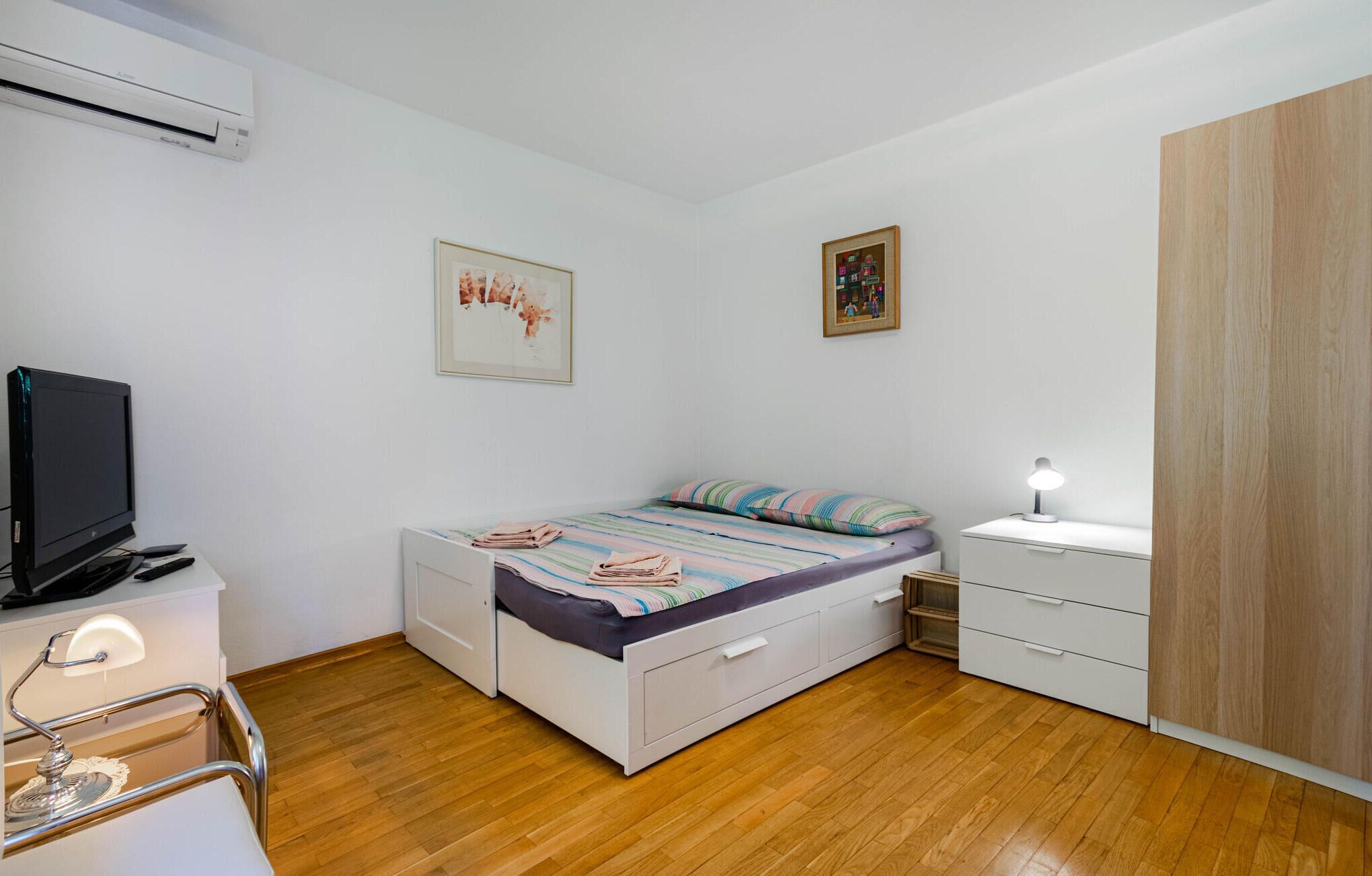 Un dormitorio con cama, escritorio con lámpara, televisor y armario.