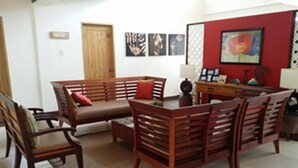A living room with a wooden sofa set, a coffee table, and a dining table with chairs. There are wall art pieces and a red accent wall. - Palm Seaside Inn and Beach Resort (Medellin)