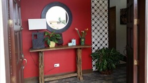 A red wall with a round mirror, a small shelf with decorative items, and a potted plant. - Palm Seaside Inn and Beach Resort (Medellin)