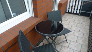 Een terras met een ronde tafel en twee stoelen, een bakstenen muur en een witte schutting.