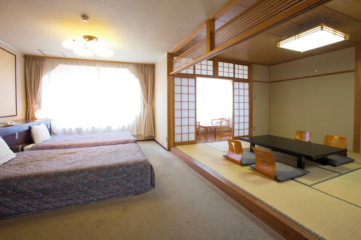 A traditional Japanese-style room with tatami flooring, a low table with cushions, and a sliding door leading to a balcony.