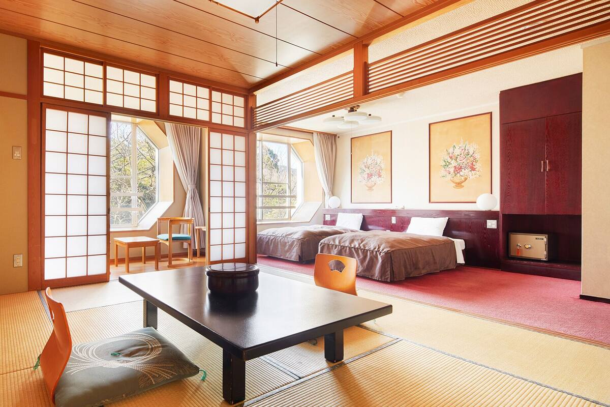 A traditional Japanese-style room with tatami flooring, a low table, a sofa, and a bed.