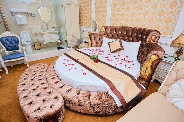 A luxurious bedroom with a large bed, a tufted ottoman, and a classic chair.