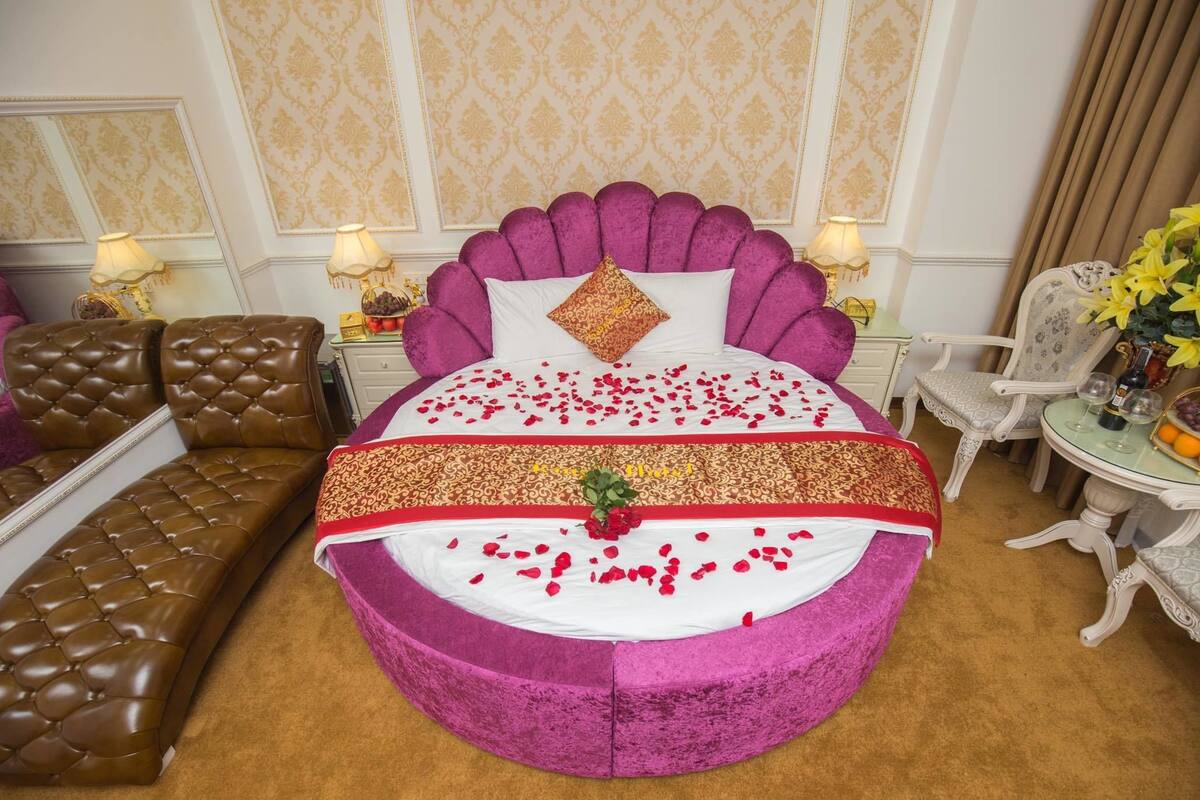 A luxurious bedroom with a large bed, a chaise lounge, and a small table with flowers.