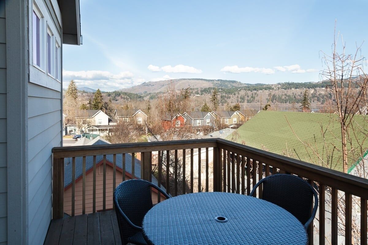 A balcony with a table and chairs, overlooking a residential area with houses and a green field.
