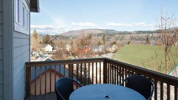 A balcony with a table and chairs, overlooking a residential area with houses and a green field.