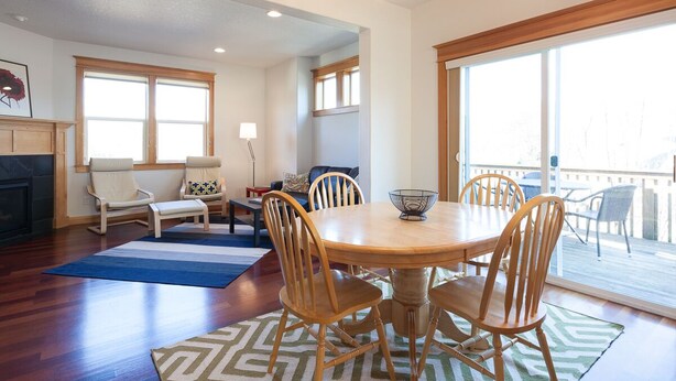 A dining area with a round wooden table, six wooden chairs, and a chandelier. There is a fireplace, a sofa, and a window with a view of the outdoors. - Private Reserve 3 Bedroom Townhouse by RedAwning (Hood River)