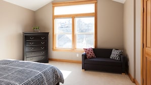 A bedroom with a large window, a dark dresser, a black sofa, and a bed with patterned bedding. - Private Reserve 3 Bedroom Townhouse by RedAwning (Hood River)