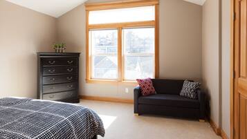A bedroom with a large window, a dark dresser, a black sofa, and a bed with patterned bedding.