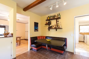 Um espaço de estar num canto com uma mesa e um banco, uma estante para bebidas fixada na parede e um quadro.