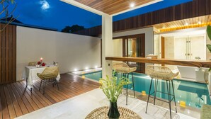 Uma área de piscina moderna ao ar livre com um deck de madeira, espreguiçadeiras e um espaço para refeições.