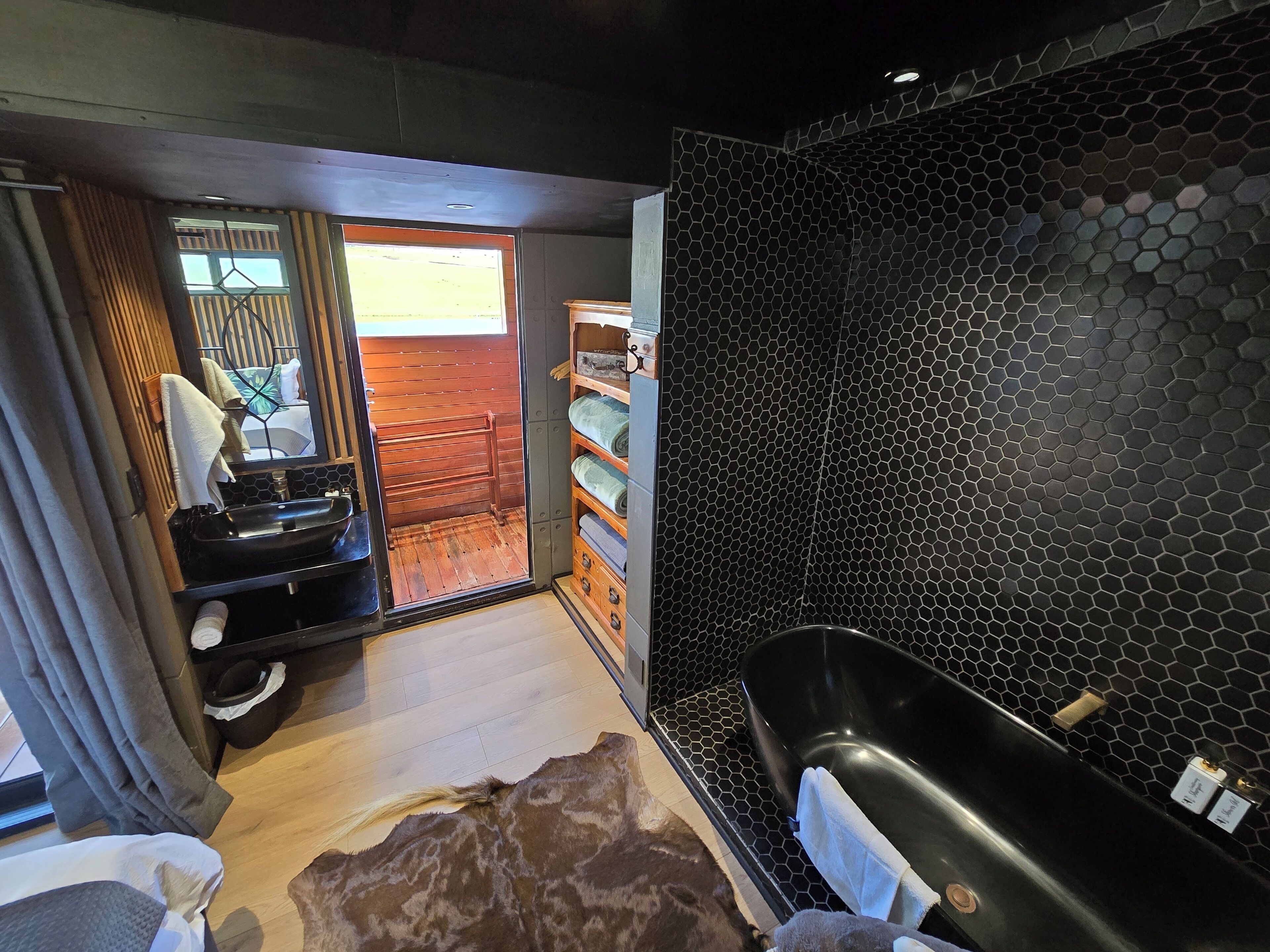 A modern bathroom with a large black bathtub, a wooden vanity, and a glass-enclosed shower area.