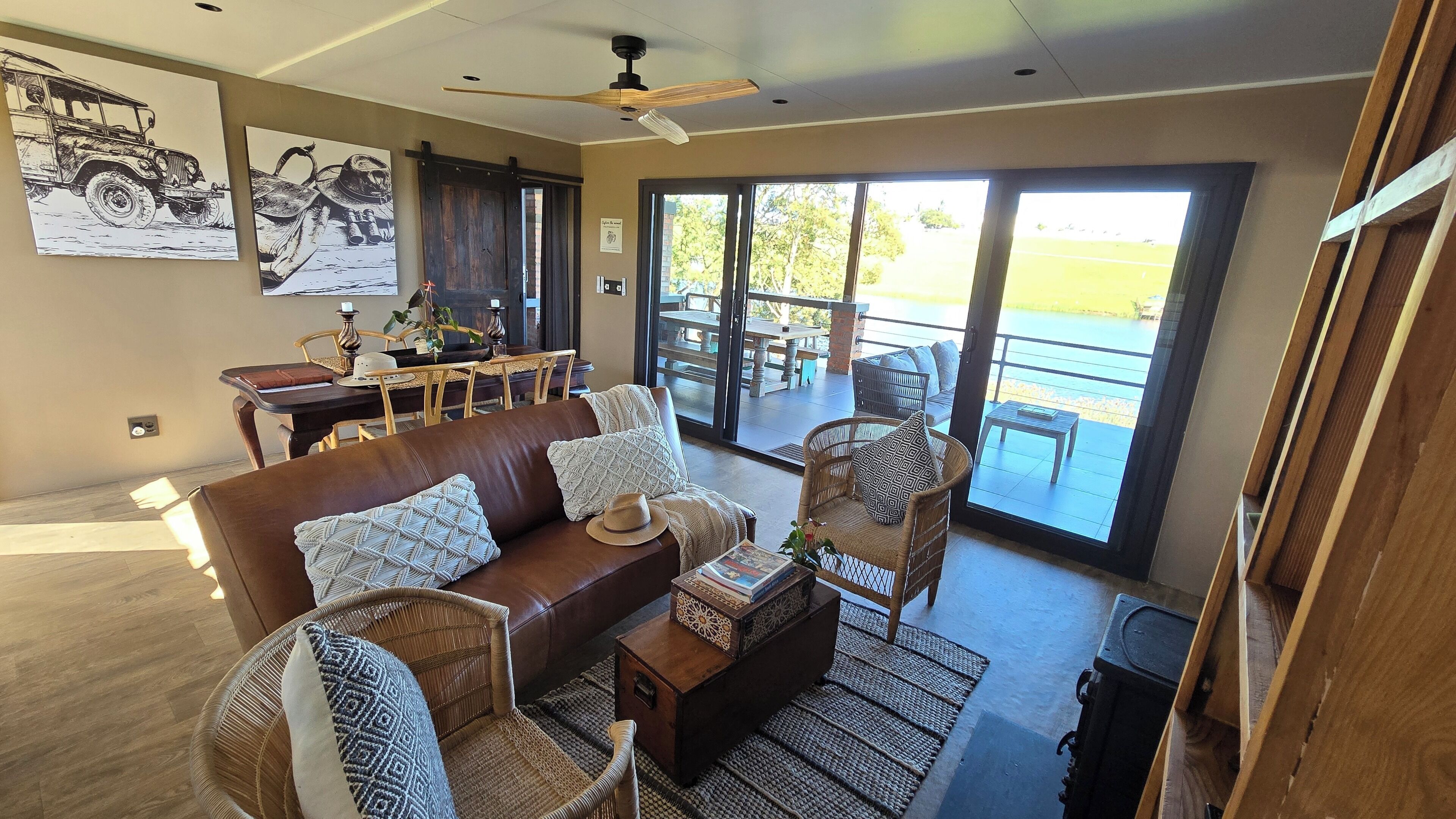 A spacious living area with a leather sofa, wicker chairs, a dining table, and a large sliding glass door leading to an outdoor patio.