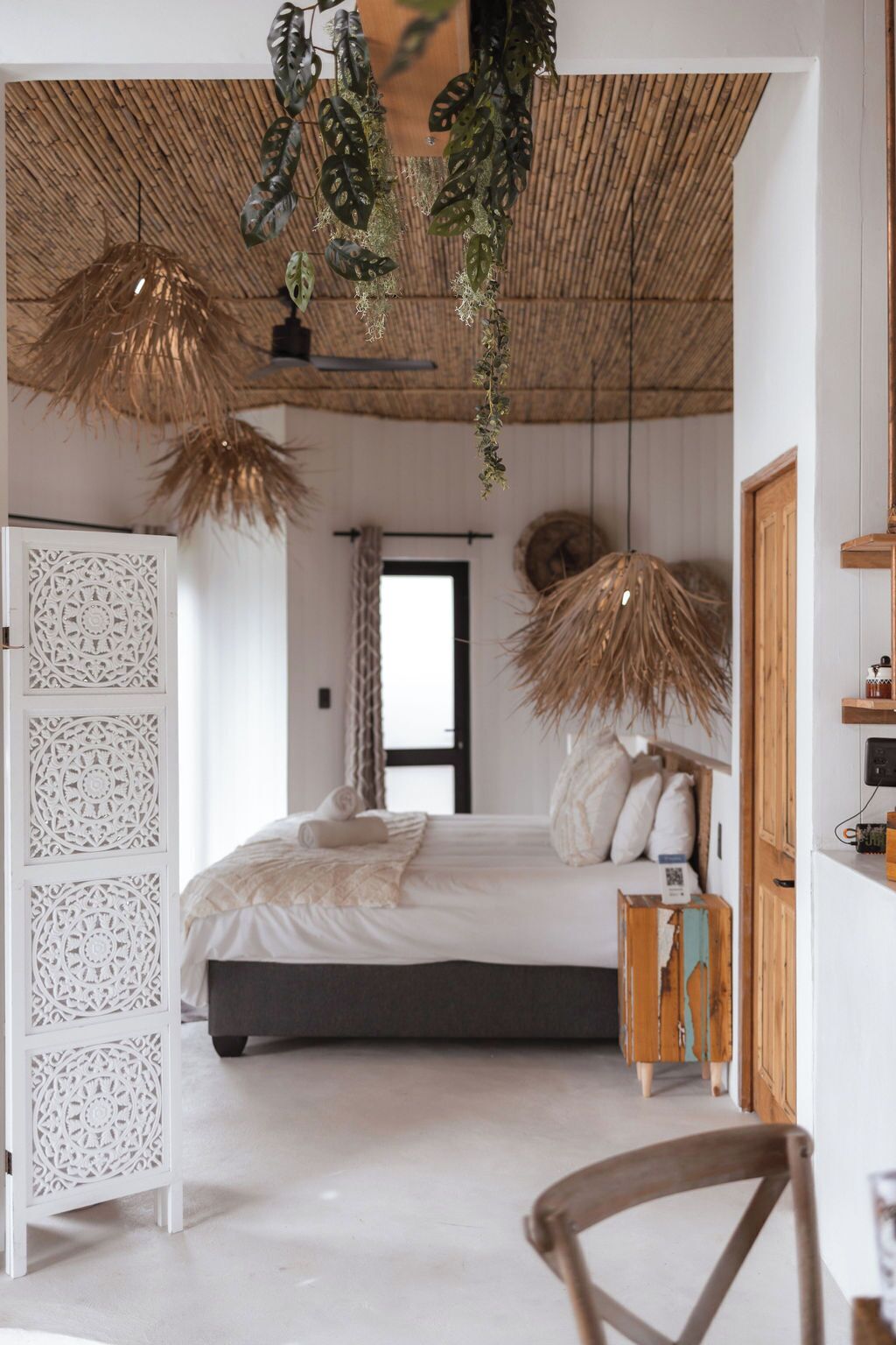 A bedroom with a bed, a white wardrobe, a wooden cabinet, and hanging plants.
