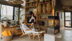 Un amplio salón con una chimenea grande, muebles de mimbre y vistas a través de un ventanal.