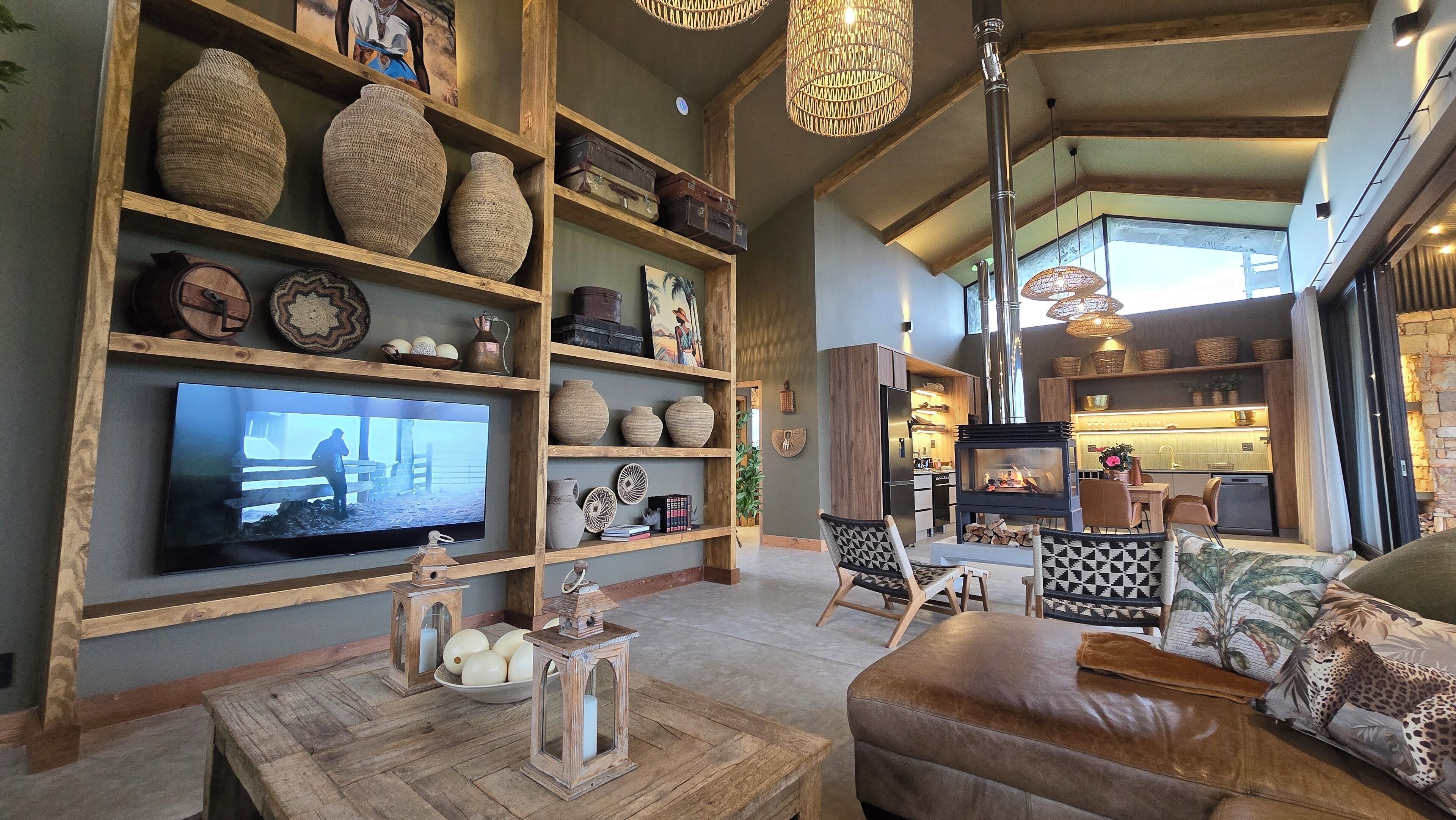 A cozy living room with a large flat-screen TV, wooden shelves with decorative items, a fireplace, and a comfortable seating area.