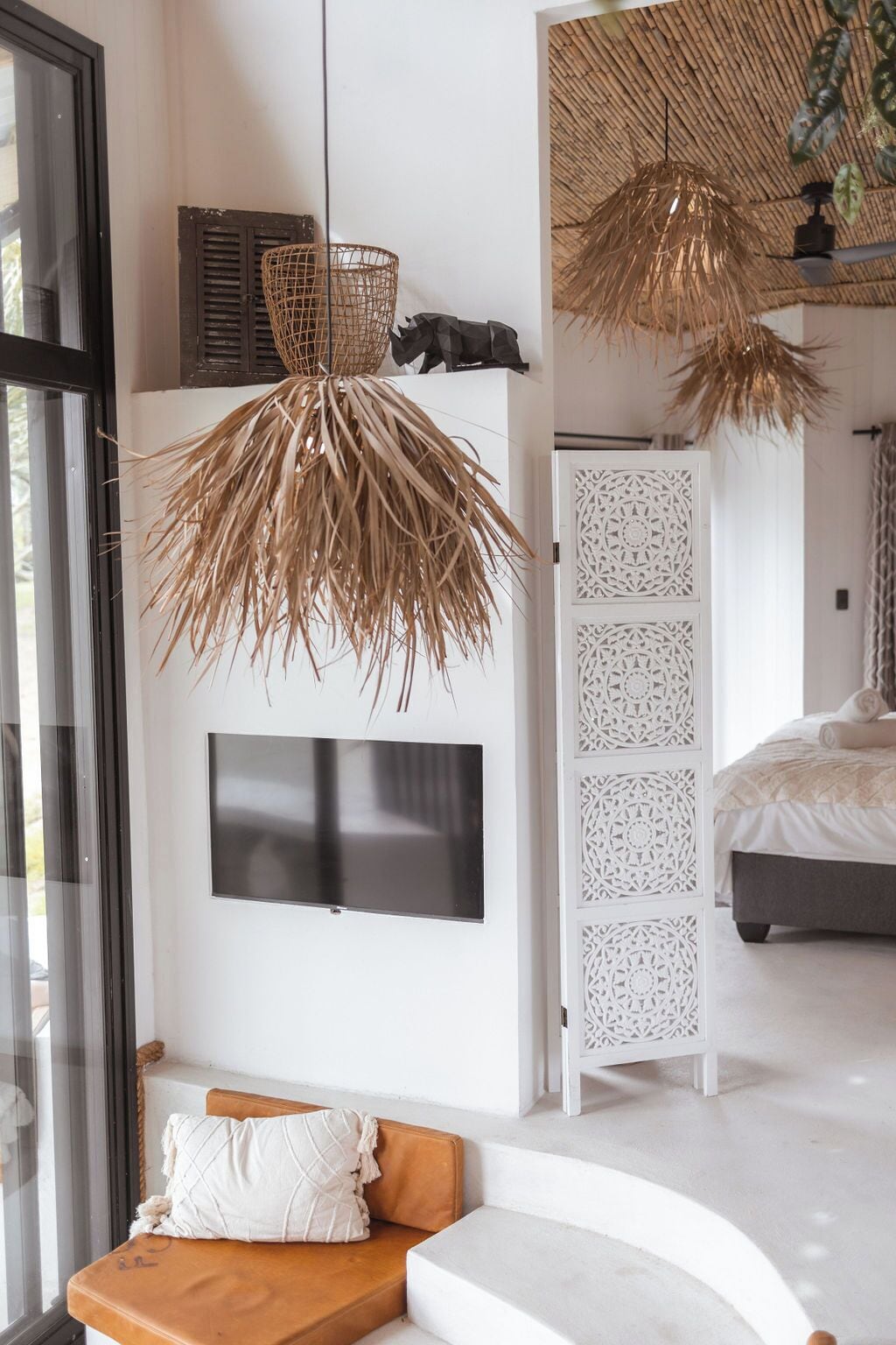 A modern bedroom with a large bed, a TV mounted on the wall, and a woven ceiling light fixture.