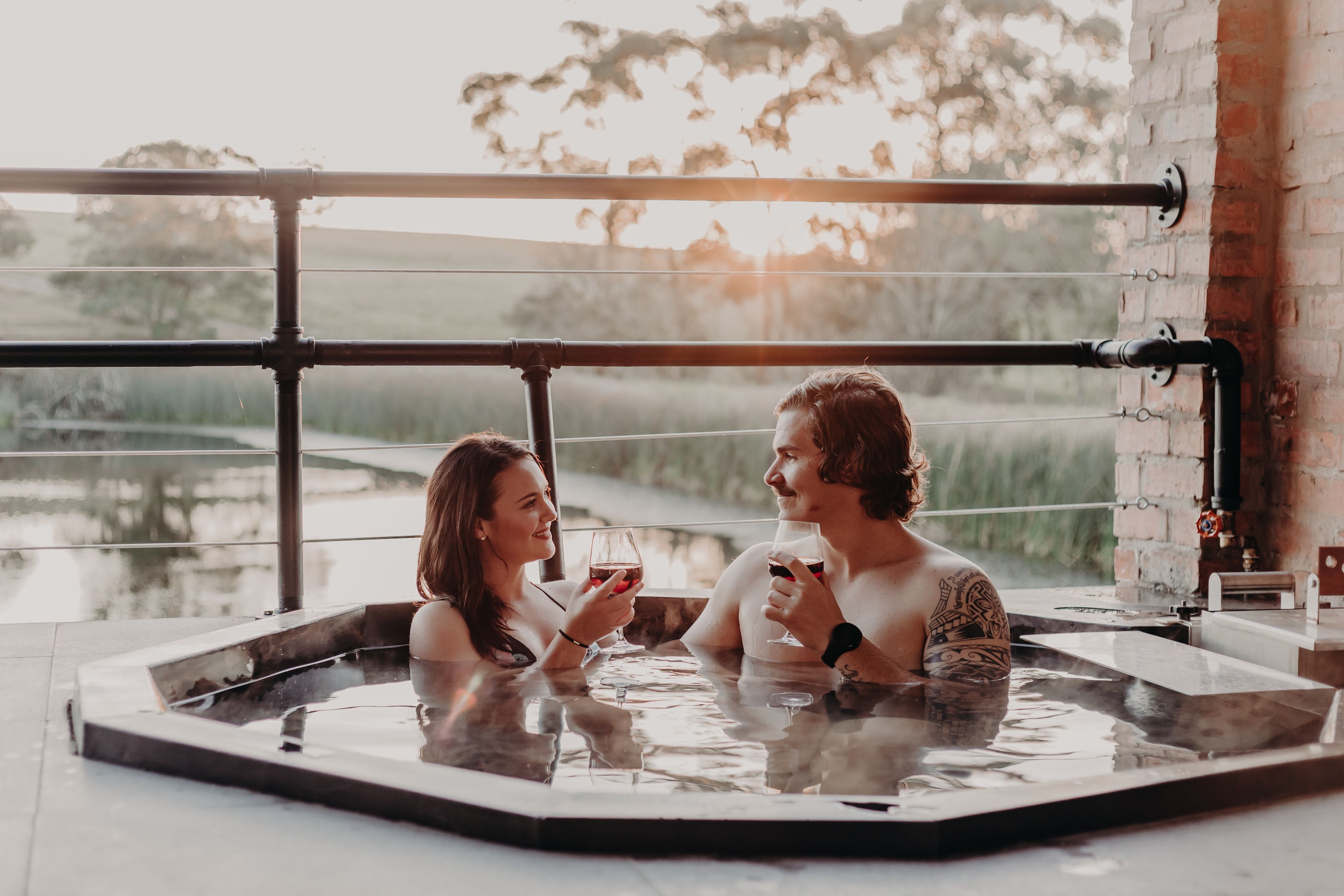 Ein Paar entspannt in einer Hot-Tub mit Blick auf ein Gewässer und Bäume.