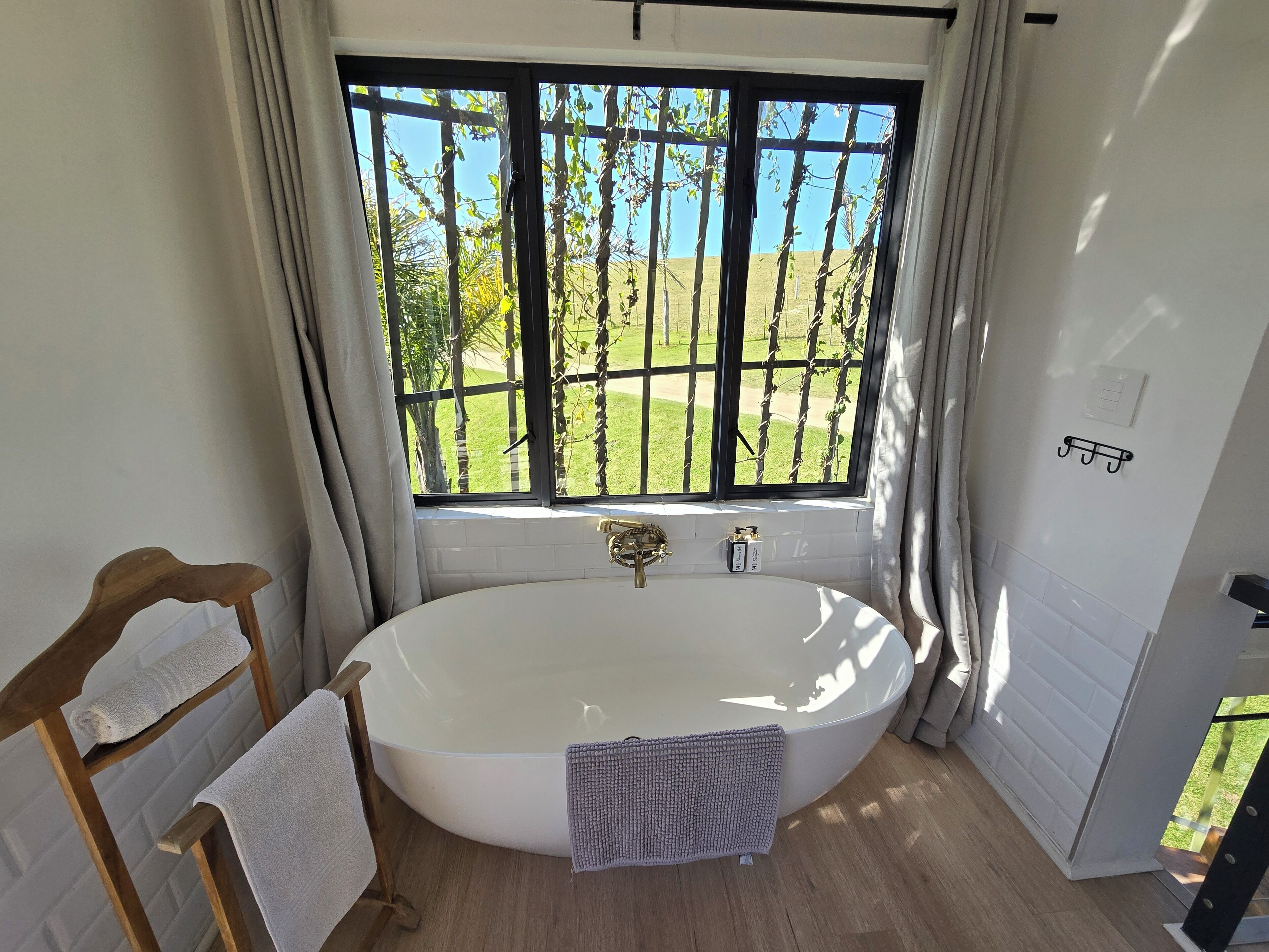 Une salle de bain avec une grande baignoire, une chaise en bois, un porte-serviettes et une fenêtre donnant sur un paysage verdoyant.