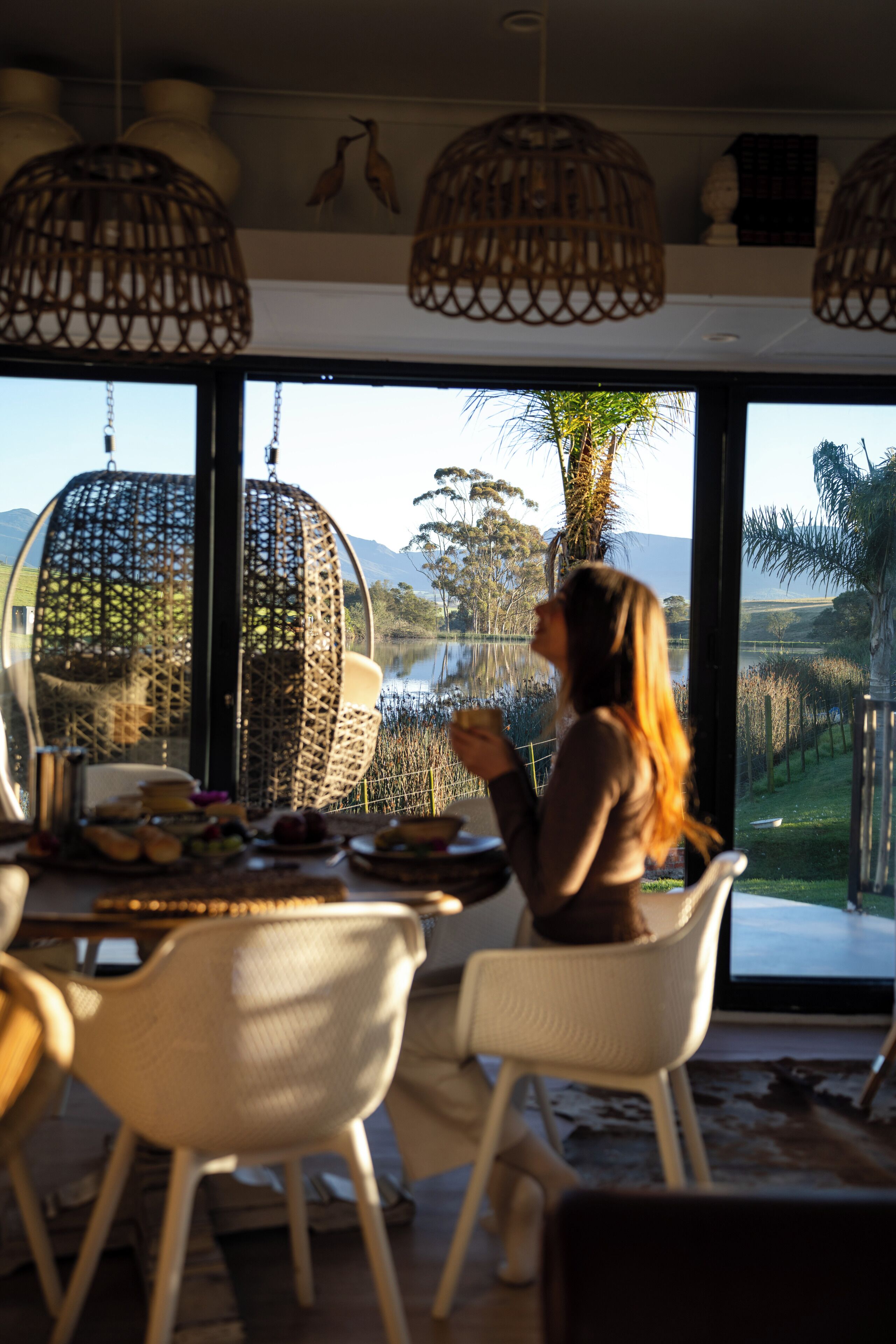 A dining area with wicker chairs and a table set for two, overlooking a lake and mountains.