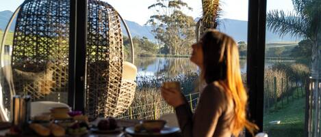 A dining area with wicker chairs and a table set for two, overlooking a lake and mountains.