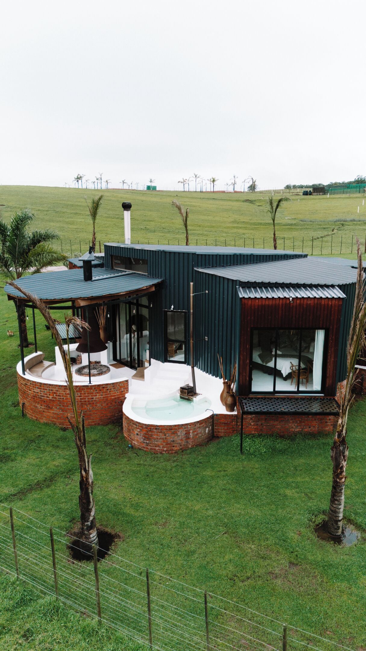A modern house with a curved brick patio, a covered seating area, and a large window overlooking a grassy field.