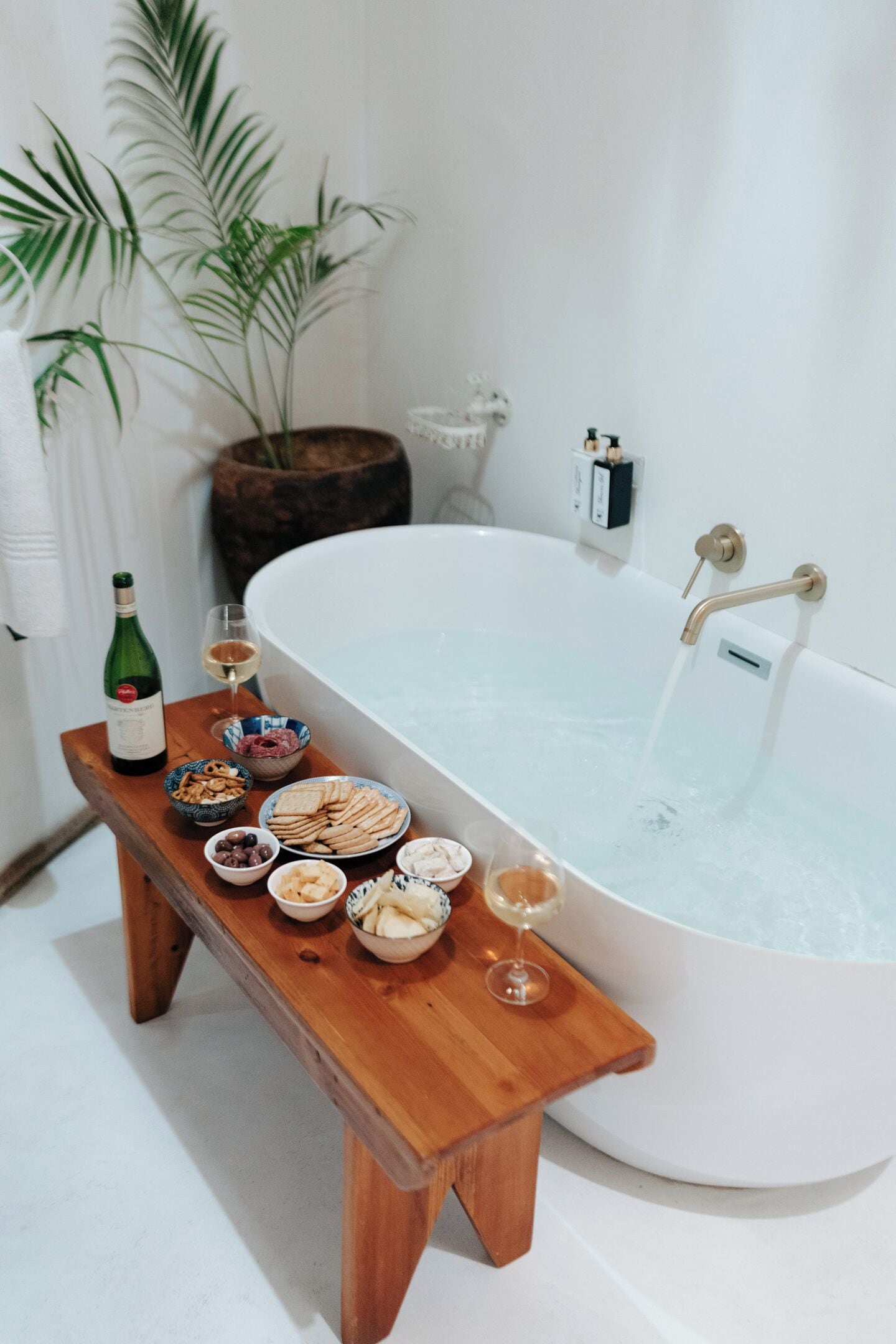 A wooden bench with snacks and drinks in front of a bathtub.
