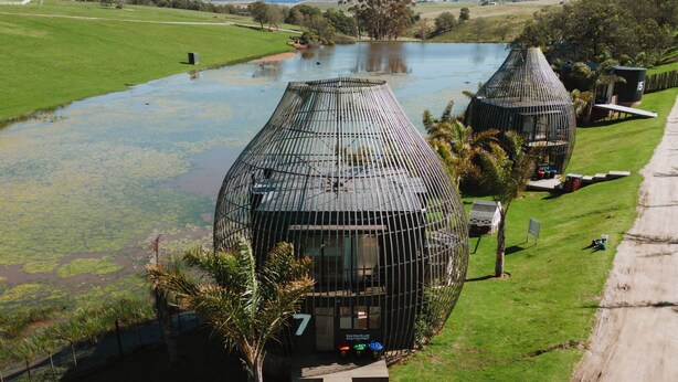 Un edificio esférico moderno con un diseño singular, rodeado de abundante vegetación y una masa de agua.