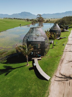 A modern spherical building with a unique design, surrounded by lush greenery and a body of water. - Buff & Fellow Eco Cabins (George)