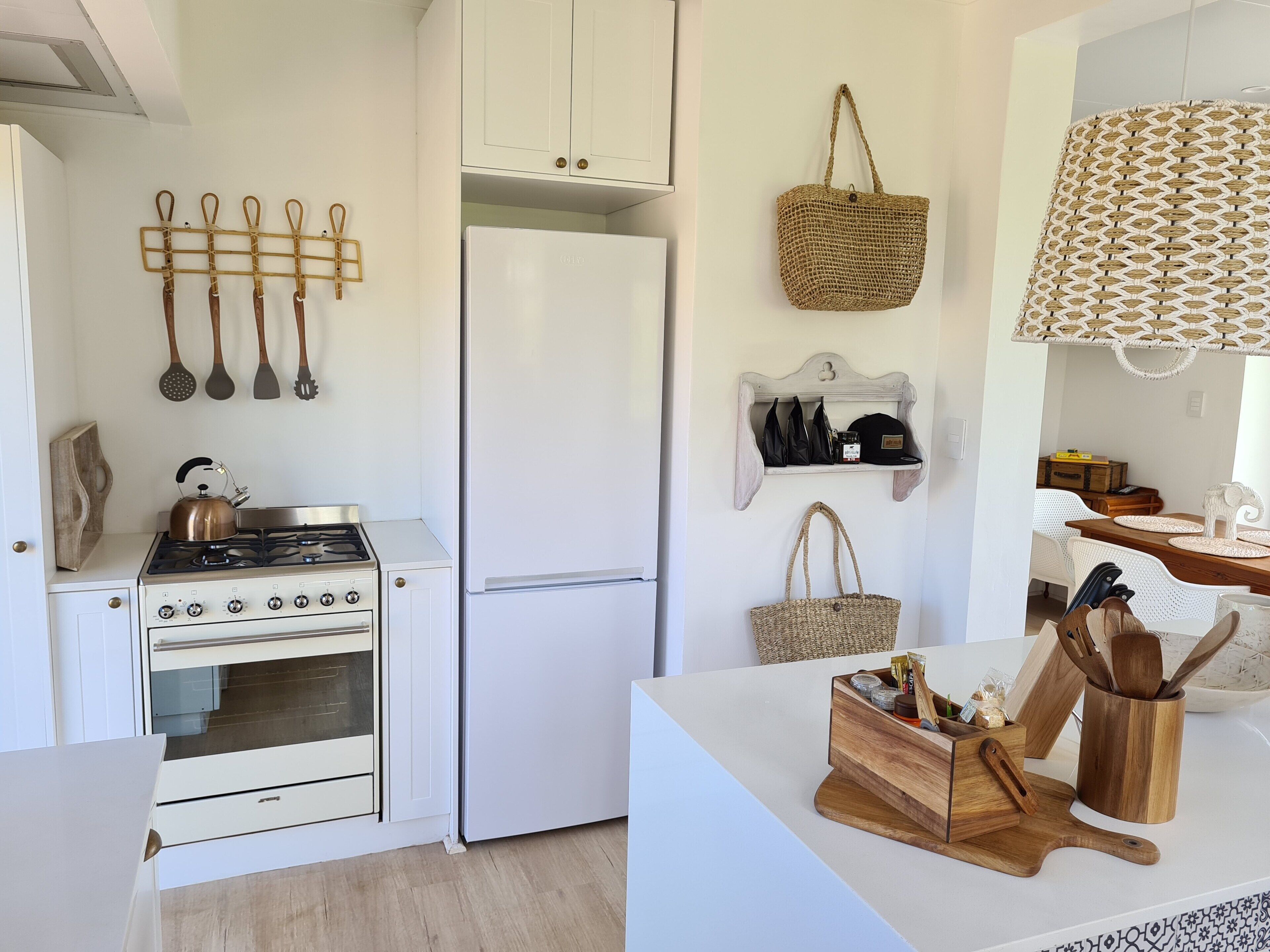 Una cocina con armarios blancos, una estufa a gas, un refrigerador y un especiero colgante.
