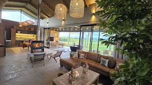 A spacious living area with a fireplace, comfortable seating, and large windows offering a view of the outdoors. - Buff & Fellow Eco Cabins (George)