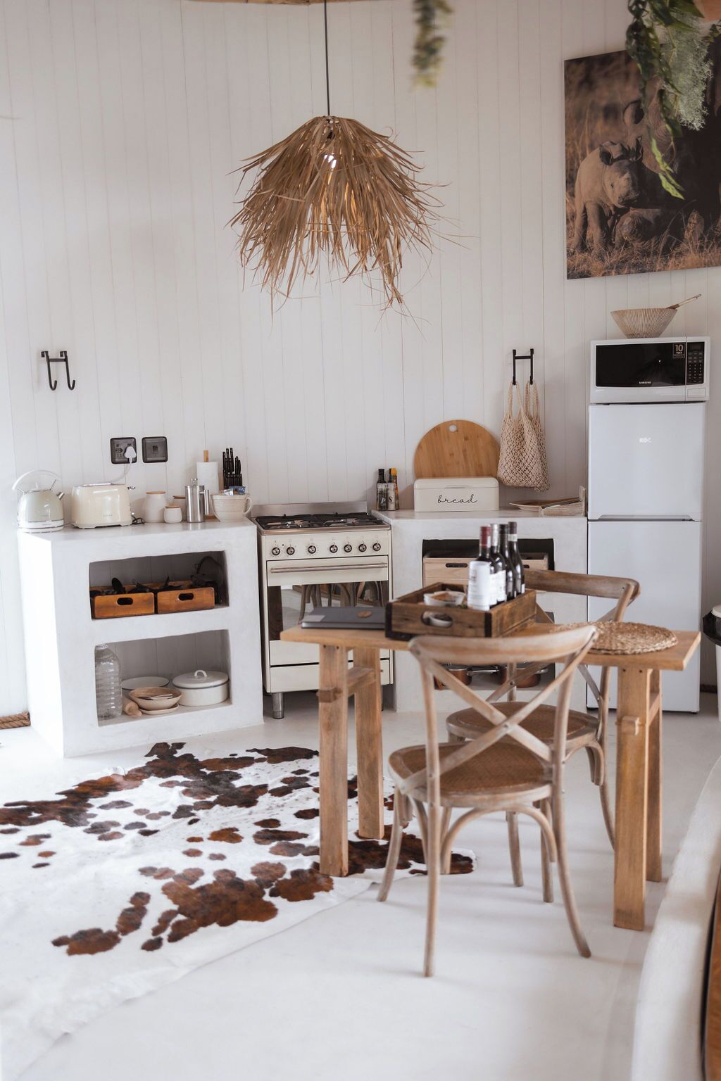 Una cocina moderna con armarios blancos, una mesa de comedor de madera y un tapete de cuero de vaca.