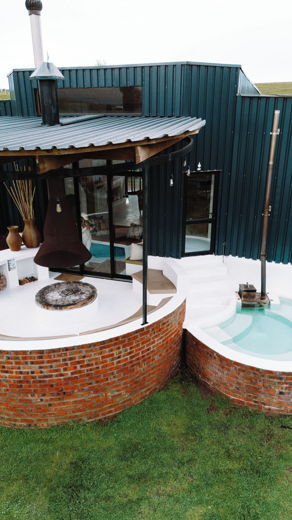 Un espacio de estar al aire libre con forma circular, con pared de ladrillo, pérgola de madera y un jacuzzi.