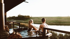 Una pareja en un jacuzzi con vista a un cuerpo de agua y un campo de césped al fondo.