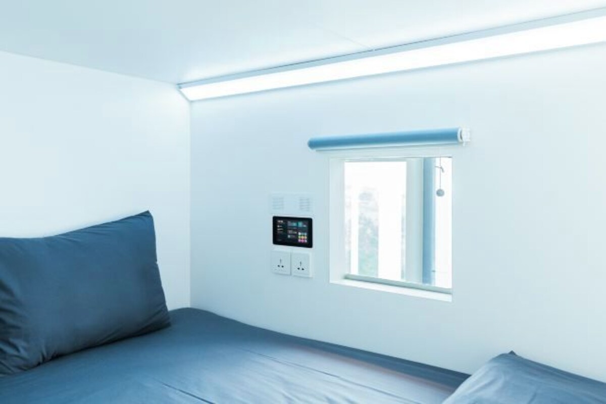 Ein Zimmer mit einem Bett, einem Fenster und einer Bedienkonsole an der Wand.