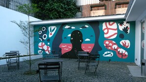 Un área exterior con mesas y sillas, un mural en la pared y piso de grava.