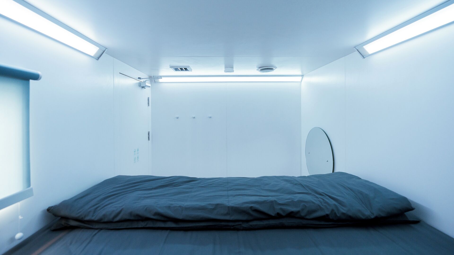 A compact, modern room with a single bed, a small mirror, and a door.