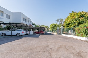 Un’area di parcheggio con due automobili, un carportal coperto e un edificio dalla facciata bianca.